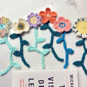 May include: Six crocheted flower bookmarks with green stems. The flowers are in various colors, including pink, yellow, blue, and purple.