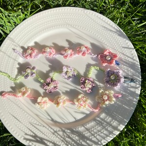 May include: Three crocheted flower hair clips with pearl accents. The clips are in shades of pink, purple, and cream.