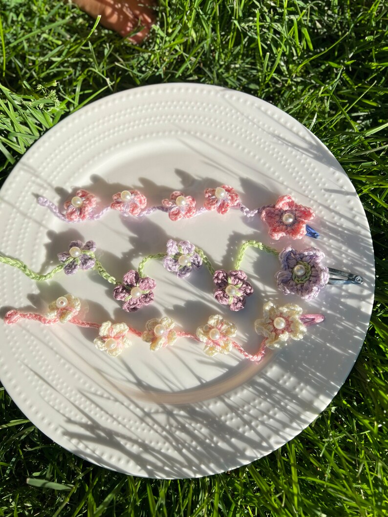 May include: Three crocheted flower hair clips with pearl accents. The clips are in shades of pink, purple, and cream.