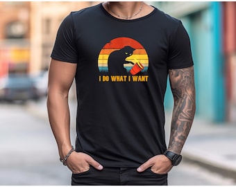 May include: Black t-shirt featuring a cat silhouette with a red cup, set against a retro sunset design. The text "I DO WHAT I WANT" is printed below the graphic. The shirt is made of a soft material.