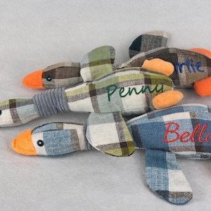 May include: Four plaid fabric duck toys with orange beaks and feet. Each duck has a different name embroidered on it: Charlie, Penny, and Bella. The ducks are made of a plaid fabric in shades of blue, green, and brown.