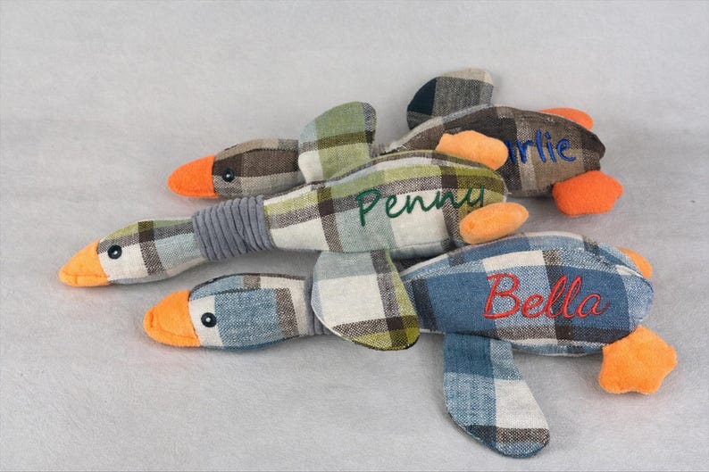 May include: Four plaid fabric duck toys with orange beaks and feet. Each duck has a different name embroidered on it: Charlie, Penny, and Bella. The ducks are made of a plaid fabric in shades of blue, green, and brown.