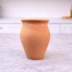 May include: A terracotta-colored vase with a wide, slightly flared rim and a rounded body. The vase has a smooth, unglazed surface and a classic, rustic appearance. It is suitable for displaying flowers or as a decorative accent.