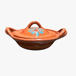 May include: A small, terracotta-colored ceramic cooking pot with a lid. The lid features a blue and red floral design. The pot has two side handles and a handle on the lid. This traditional cookware is ideal for serving soups and stews.
