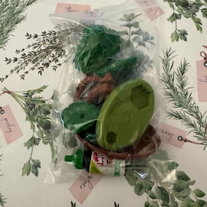 May include: A clear plastic bag containing green and brown plastic toy trees, a brown plastic toy boat, and a small green bottle labelled "Mini Brown" and "Mushroom Mix".