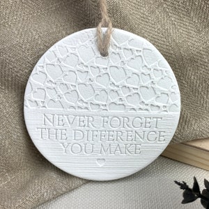 May include: White ceramic ornament with a heart pattern and the text "Never forget the difference you make".