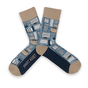 May include: A pair of blue socks with a brown cuff. The socks feature a pattern of office supplies, including a computer, a calendar, a stapler, and a pencil. The text "SMART ASSET" is printed on the bottom of one sock.