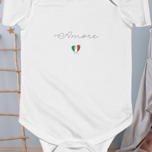 May include: White baby onesie with the word "Amore" in cursive script and a heart-shaped Italian flag design.