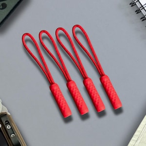 May include: Four red zipper pulls, each featuring a textured, cylindrical grip attached to a looped cord. The pulls are arranged in a parallel row, showcasing a consistent design with a diamond-patterned surface on the rubberized ends.