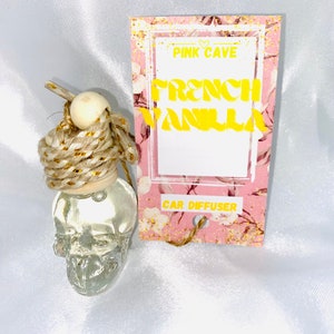 May include: A glass skull-shaped car diffuser with a pink and white floral tag that reads "Pink Cave French Vanilla Car Diffuser".