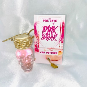 May include: A pink skull-shaped car air freshener with a woven top and a card that reads "Pink Cave Pink Sugar Car Diffuser". The air freshener is attached to a small gold-colored charm.
