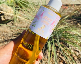 May include: A clear glass bottle with a white pump dispenser filled with a yellow liquid. The bottle has a pink and white label with the text "Peach Vanilla Body Oil 120 ml / 4 fl oz".