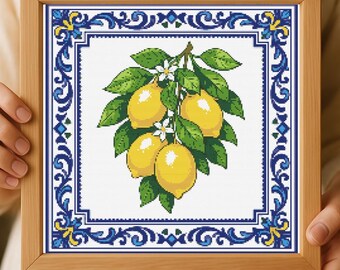 May include: A framed cross-stitch artwork depicting a lemon branch with yellow lemons, green leaves, and white flowers. The artwork is framed by a blue and white decorative border, set in a light brown wooden frame.