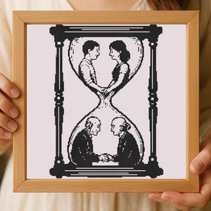 Può includere: Un'opera d'arte a punto croce incorniciata con un design a clessidra in bianco e nero. La clessidra contiene due coppie, una giovane e una più anziana, che si tengono per mano. La cornice è in legno marrone chiaro.