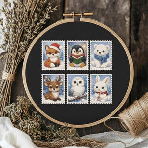 May include: A black embroidery hoop holds six postage stamp-style cross-stitch designs featuring winter animals. A fox in a Santa hat, a penguin reading, a polar bear in a scarf, a deer, an owl, and a rabbit in a scarf are depicted.
