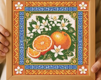 May include: Cross-stitch artwork in a wooden frame depicting oranges, orange blossoms, and green leaves. The artwork has a decorative border with blue, orange, and white geometric patterns. The frame is held by a person.