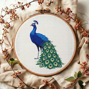 May include: A cross-stitch peacock design in a wooden embroidery hoop. The peacock is rendered in shades of blue and green, with a detailed tail. The background is white, and the hoop is surrounded by decorative branches.
