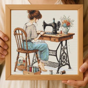 Puede incluir: Una impresión enmarcada representa a una mujer cosiendo en una máquina de coser vintage. La escena incluye una mesa de madera, una silla y un jarrón con flores. También son visibles carretes de hilo y una cesta. La obra de arte está en una paleta de colores cálidos.
