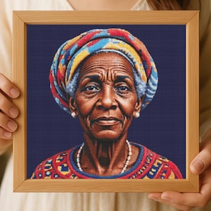 Puede incluir: Retrato en punto de cruz enmarcado de una anciana con un pañuelo en la cabeza colorido y una parte superior estampada. El retrato está sobre un fondo azul oscuro y enmarcado en madera marrón claro. La mujer lleva pendientes de perlas y un collar de perlas.
