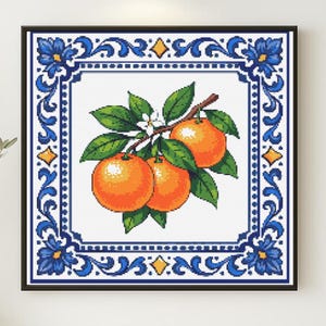 May include: Cross-stitch artwork depicting oranges on a branch with green leaves and white blossoms. The oranges are set against a white background, framed by a blue and white decorative border in a black frame.