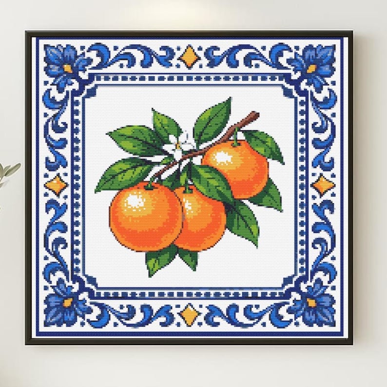 May include: Cross-stitch artwork depicting oranges on a branch with green leaves and white blossoms. The oranges are set against a white background, framed by a blue and white decorative border in a black frame.