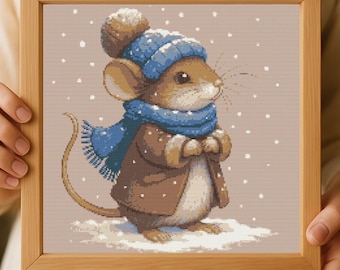 May include: A framed cross-stitch of a mouse in winter attire. The mouse wears a blue knit hat, scarf, and brown coat, standing in snow. The artwork is in a wooden frame, with a neutral background and falling snowflakes.