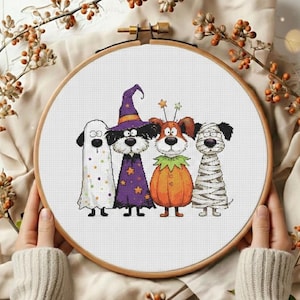 May include: A Halloween-themed cross-stitch design featuring four dogs in costumes: a ghost, a witch, a pumpkin, and a mummy. The design is set in a wooden embroidery hoop, perfect for seasonal decor.