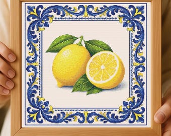 May include: Cross-stitch artwork featuring two lemons with green leaves, one whole and one sliced, on a white background. The piece is framed with a wooden border and a blue and yellow decorative border.