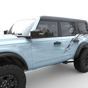 May include: A light blue Ford Bronco with black accents and a black roof. The vehicle has black side mirrors and black door handles. The vehicle has a black and white graphic on the side.