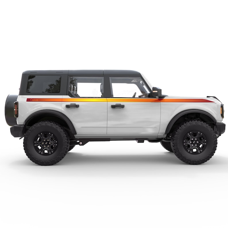 May include: White Ford Bronco with a black roof and orange and red racing stripes along the side. The vehicle is shown in profile view.