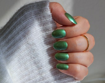 Op de afbeelding: Een hand met groene glitternagellak op alle vijf vingernagels. De hand draagt een gouden ring aan de ringvinger.