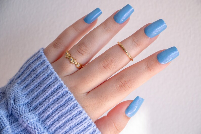 Op de afbeelding: Een hand met lichtblauwe nagellak op elke vinger. De hand draagt twee gouden ringen.