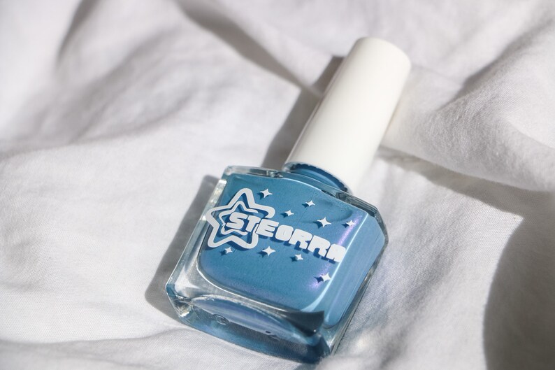 Op de afbeelding: Een flesje blauwe nagellak met een witte ster en het woord "STEORRA" op het etiket.