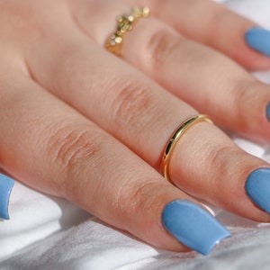 Op de afbeelding: Een hand met lichtblauwe nagellak op elke vinger. De hand draagt twee gouden ringen.