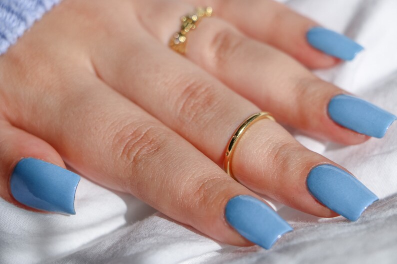Op de afbeelding: Een hand met lichtblauwe nagellak op elke vinger. De hand draagt twee gouden ringen.