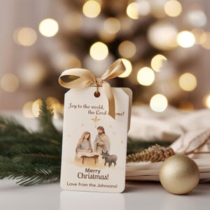 Pode incluir: Uma etiqueta de presente de Natal creme com um laço de fita dourada. A etiqueta apresenta uma ilustração da natividade e o texto "Joy to the world, the Lord is come!" e "Merry Christmas!" com uma mensagem personalizada.