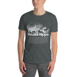 May include: Dark grey t-shirt featuring a white illustration of a hippo and the words "House Hippo." Below the graphic is a paragraph of text. The t-shirt is made of a soft material.