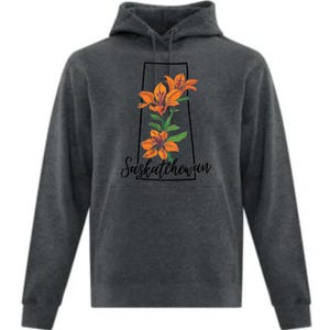May include: A charcoal grey hooded sweatshirt with a floral design. The design features orange lilies and green leaves within a black frame, with the word "Saskatchewan" in cursive script below.