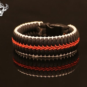 May include: Black paracord bracelet with white and red stitching. The bracelet has a black buckle closure.