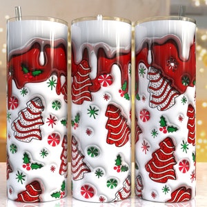 Könnte beinhalten: Drei weiße Becher mit roten und weißen Weihnachtsbaummotiven und rotem Zuckerguss, der an den Seiten heruntertropft. Die Becher haben einen weißen Hintergrund mit grünen Stechpalmenblättern und roten Beeren.