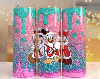 May include: Three pink and turquoise glitter tumblers with a Christmas theme. The tumblers feature Mickey Mouse, Donald Duck, and Daisy Duck dressed in Santa suits. The tumblers have a dripping turquoise glitter design and snowflakes.