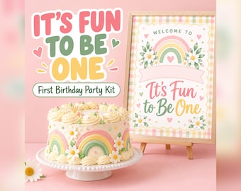 May include: A first birthday party kit featuring a round cake with white frosting, rainbow decorations, and daisy accents on a white stand. Next to it is a framed sign with a rainbow, flowers, and the text "Welcome to It's Fun to Be One."