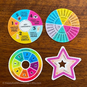 May include: Four colourful cards, circular and star-shaped, with text and illustrations. The cards include phrases like "Get Grounded", "Calm Down", and "Breathe". The cards are on a wooden surface.