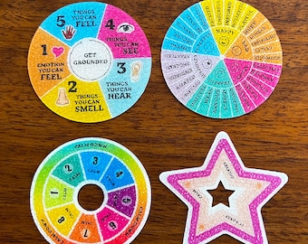 May include: Four colorful, circular and star-shaped cards with text and illustrations. The cards include phrases like "Get Grounded", "Calm Down", and "Breathe". The cards are on a wooden surface.