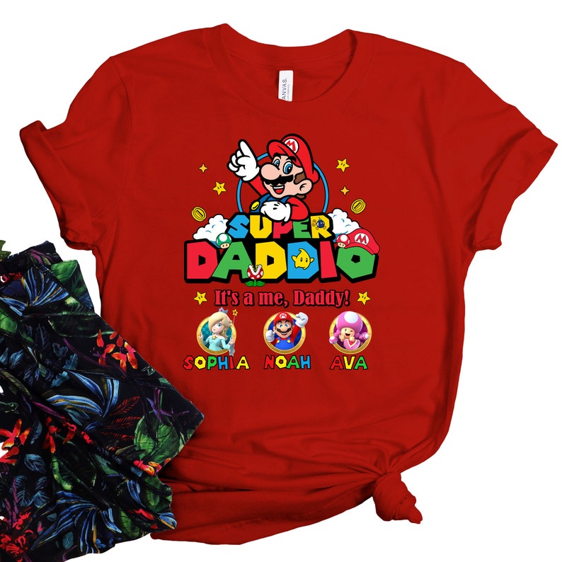 May include: Red t-shirt with a Super Daddi graphic featuring Mario, Luigi, Peach, and Toad. The text says "It's a me, Daddy!" and includes the names Sophia, Noah, and Ava.