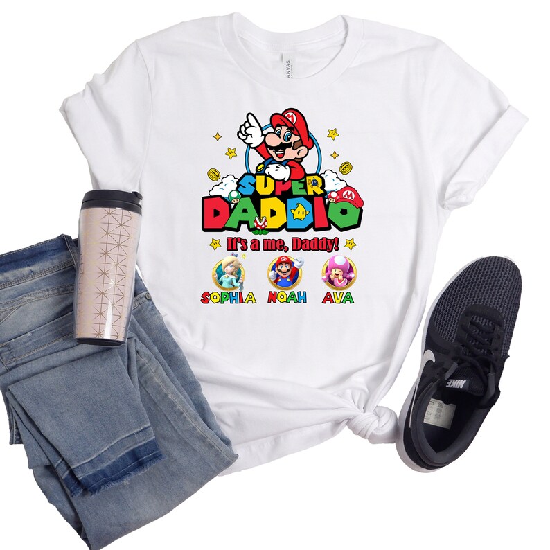 May include: White t-shirt with a Super Daddo graphic featuring a cartoon Mario character. The text "It's a me, Daddy!" is printed below the graphic. Three smaller circles with cartoon characters and the names Sophia, Noah, and Ava are printed below the text.