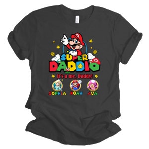 May include: A dark grey t-shirt with a Super Daddi design featuring a cartoon Mario character. The text "It's a me, Daddy!" is printed below the character. Three smaller cartoon characters are printed below the text, with the names Sophia, Noah, and Ava printed below each character.