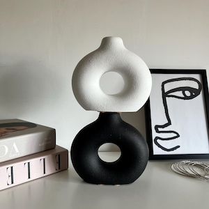 May include: A white ceramic vase with a ring-shaped opening, stacked on top of a black ceramic vase with a similar ring-shaped opening.