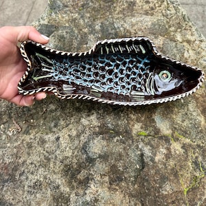 May include: A brown ceramic fish-shaped serving dish with a blue and white glaze. The dish has a detailed design of scales and a large eye.