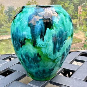 May include: A bulbous ceramic vase featuring a glossy glaze with a marbled pattern of deep emerald green, vibrant turquoise, and dark navy blue. The surface displays a fine crackle texture throughout, with a smooth, rounded rim and base.